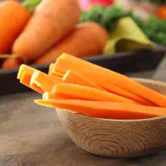 Marchewka pokrojona w słupki w drewnianej miseczce. W tle całe marchewki. Zastanawiasz się, ile kalorii ma marchewka gotowana, a ile surowa?