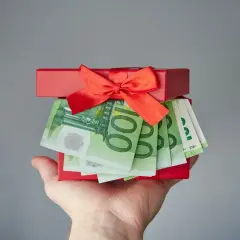 Czerwone pudełko z prezentem i banknotami euro na dłoni.