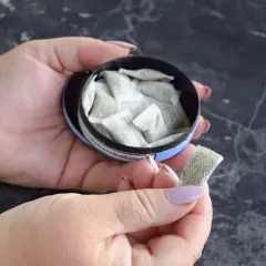 Dłonie trzymają puszkę z białymi woreczkami. To snus, tytoń do ust.