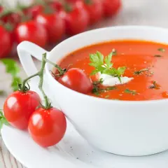 Zupa pomidorowa, ozdobiona gałązką pomidorków i natką pietruszki, wygląda apetycznie. Ile waży zupa pomidorowa? To zależy od porcji!