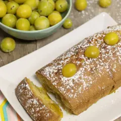 Gâteau lorrain aux mirabelles, saupoudré de sucre glace, avec des mirabelles fraîches sur le dessus et dans une coupelle à côté.