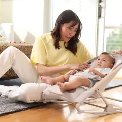 En kvinna sitter på golvet bredvid en bebis i en babysitter från Maxi-Cosi.