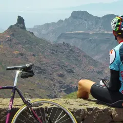 Ciclista descansa tras explorar rutas en bici Gran Canaria. Paisaje montañoso y su bicicleta morada.