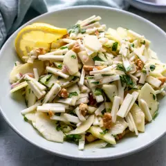 Ein frischer Staudensellerie Salat italienisch mit Äpfeln, Walnüssen und Kräutern, garniert mit einer Zitronenspalte.