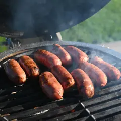 Mehrere Salsiccia brutzeln auf einem Grill. Rauch steigt auf und die Würste bekommen schöne Grillstreifen.