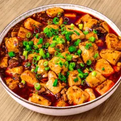 En skål med kryddig mapo tofu, toppad med färsk salladslök, serverad på ett träbord.