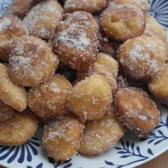 Montón de buñuelos de manzana dorados y espolvoreados con azúcar, servidos en un plato blanco con diseño azul.