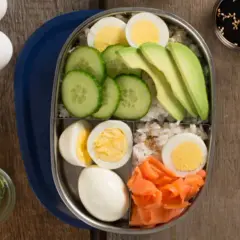 A bento box filled with rice, sliced cucumber, avocado, smoked salmon, and hard-boiled egg.