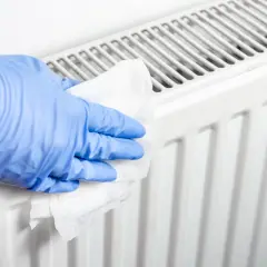 Rękawiczka w niebieskiej rękawiczce czyści biały grzejnik aluminiowy. Dowiedz się, jak wyczyścić grzejnik aluminiowy w środku.