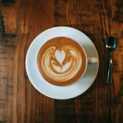 Ein Cappuccino mit Herz-Latte-Art auf einem Holztisch. Woher kommt Cappuccino? Aus Italien, natürlich!