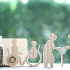 Skarbonka i drewniane figurki symbolizujące wsparcie dla osób starszych i niepełnosprawnych. To świadczenie wspierające punkty w życiu.