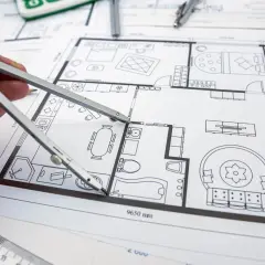 Rysunek techniczny z zaznaczonymi zmianami istotnymi w projekcie budowlanym. Dłoń z cyrklem nad planem mieszkania.
