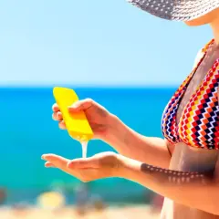 Frau trägt Sonnencreme auf, um sich vor der Sonne zu schützen. Wichtig: Sonnencreme mehrmals auftragen!