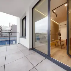 Nowoczesny balkon z płytkami, szklaną balustradą i widokiem na budynki.