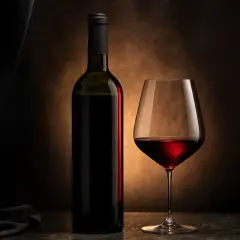 Una bottiglia e un calice di vino rosso, immersi in un'atmosfera suggestiva che esalta i profondi colori vino rosso.