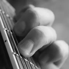 Zbliżenie na palce gitarzysty dociskające struny do gryfu.