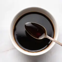 A spoon rests in a bowl of dark liquid, hinting at how to make sweet soy sauce.