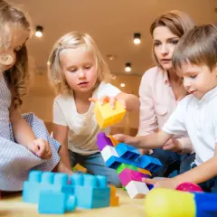 Dzień kobiet w żłobku: dzieci budują z klocków pod okiem opiekunki. Radość i kreatywność maluchów.