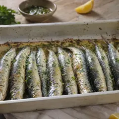 Sardinas al horno recién hechas, doradas y espolvoreadas con perejil fresco, listas para disfrutar con un toque de limón.