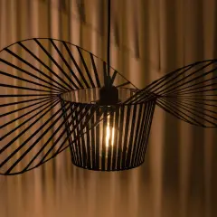 Nowoczesna lampa wisząca o nietypowym kształcie, przypominającym wachlarz lub wachlarz, tworzy ciekawe cienie na zasłonie.