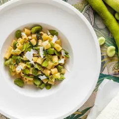 Piatto di pasta con fave fresche, un assaggio della ricetta pasta con le fave fresche alla siciliana, guarnita con ricotta salata e erbe aromatiche.