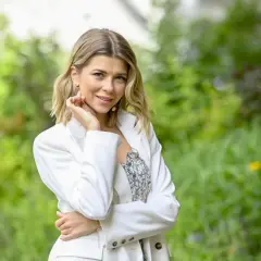 Agnieszka Dziekan z Koła Fortuny, uśmiechnięta, w białej marynarce, na tle zieleni.