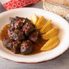 Sabrosa carne de cabra estofada en salsa con trozos de pimiento rojo y verde, acompañada de patatas gajo doradas.