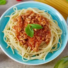 Spaghetti bolognese na talerzu, ozdobione bazylią. Idealne na prosty przepis obiadowy.
