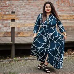 Kobieta w stylowej, granatowej sukience plus size długiej z białym wzorem, pozuje na tle ceglanej ściany i drewnianych ławek.