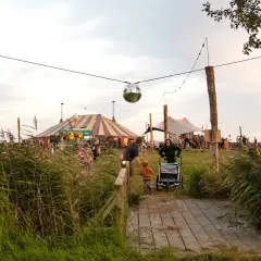 Ein buntes Zirkuszelt und Menschenmassen beim Calluna Festival. Eine Discokugel funkelt über dem Gelände.
