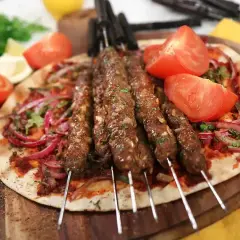 Grillad adana kebab på spett, serverad med tunnbröd, rödlök, tomat och persilja. Ett perfekt adana kebab recept för sommaren.