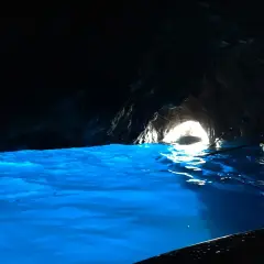 Acqua azzurra e luminosa in una grotta buia, con un'uscita illuminata dove si intravede una barca.