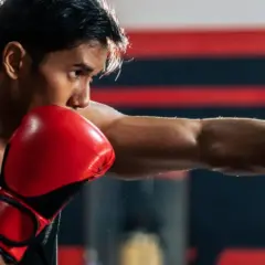 Boxer throws a powerful punch, aiming for the sternum. Red gloves flash as he trains in the ring.