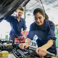 Deux mécaniciens en bleu travaillent sur un moteur de voiture, effectuant un pré contrôle technique.