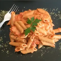 Penne w kremowym sosie pomidorowym z mascarpone, udekorowane natką pietruszki. Obok widelec i posypka z ziół.