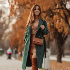 Elegancki, zielony płaszcz z bukli otula kobietę podczas jesiennego spaceru. W tle złote liście drzew.