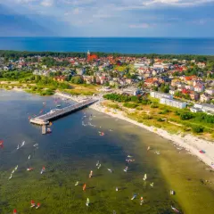 Jastarnia atrakcje dla dzieci: widok na molo, plażę i zatokę pełną żaglowców i desek windsurfingowych.