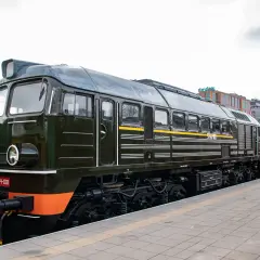 Ciemnozielona lokomotywa ST44-001, znana jako "wąsaty" lub "sztok", stoi na torach obok innych pociągów.