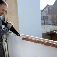 Un bricoleur prépare le cadre pour comment poser une fenêtre PVC en rénovation, sciant le bois existant.