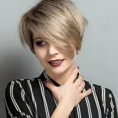 Kobieta z krótkimi blond włosami w stylu pixie, z grzywką na bok, w bluzce w paski.