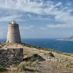 El faro de Almería se alza sobre una colina rocosa, vigilando el mar azul bajo un cielo nublado.