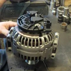 Mechanik sprawdza alternator, zastanawiając się, ile kosztuje regeneracja alternatora. W tle widać narzędzia.