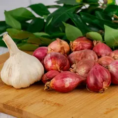Knoblauch und Schalotten auf einem Holzbrett, bereit als Hausmittel gegen Ohrenschmerzen. Grüne Blätter im Hintergrund.
