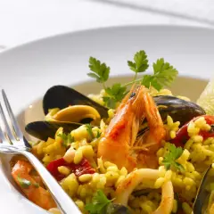 Pyszne risotto z owocami morza: krewetki, małże, kalmary i ryż, udekorowane natką pietruszki i ćwiartką limonki.