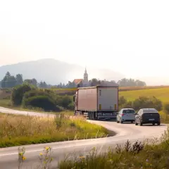 Ciężarówka i samochody na krętej drodze. Producent szuka przewoźnika, który dowiezie towar przez malownicze tereny.