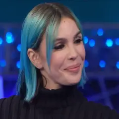 Una donna con capelli blu e neri, trucco marcato, sorride con un'espressione da rose villain.