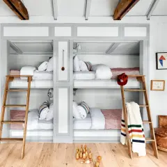 A cozy built in bunk room with four beds, wooden ladders, and playful decor like toy excavators and bowling pins.