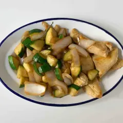 Sabroso pollo con calabacín y cebolla salteados, servido en un plato blanco con borde azul.
