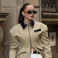 Mujer con gafas de sol y chaqueta beige con cuello negro, luciendo un look de street style impecable.