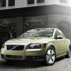 Złoty Volvo C30 segment c zaparkowany na brukowanej ulicy przed sklepem z modą.
